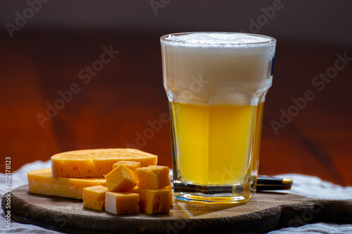 Glass of Belgian white unfiltered beer with notes of coriander and orange peer and wooden board with belgian cheese made by monks from cow milk photo