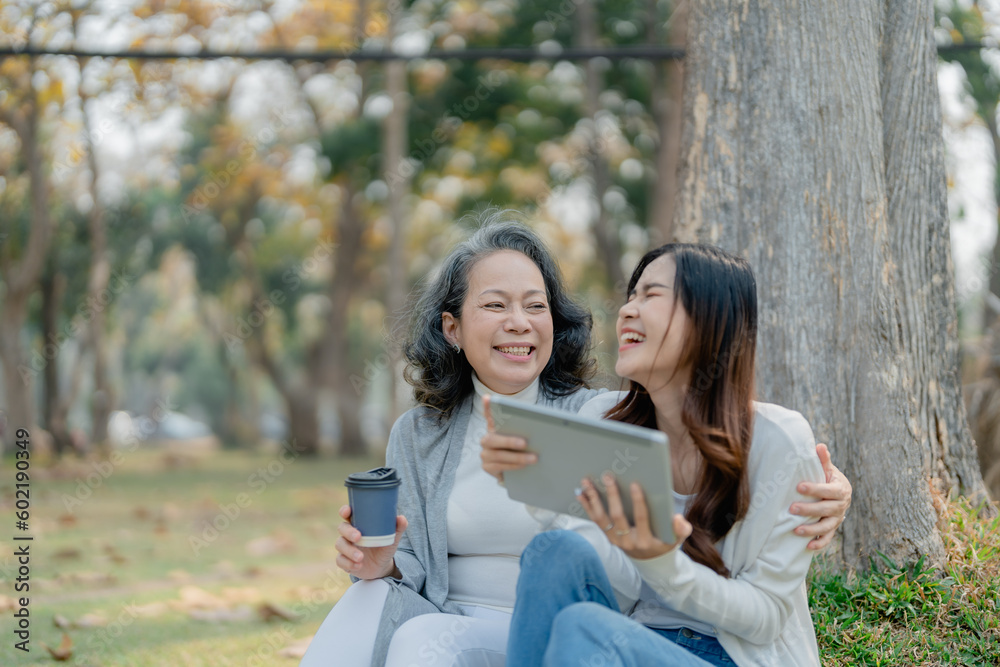 Grown daughter with aging mother expressing love and looking at tablet computer under tree in public park. Grown daughter with aging mother expressing love and looking at tablet computer under tree in public park.