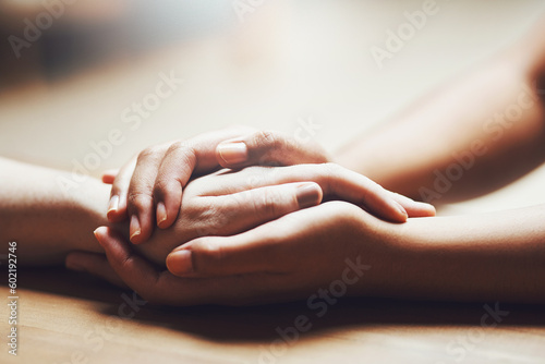 Prayer, empathy and support with people holding hands in comfort, care or understanding on a wooden table of a home. Love, faith or depression with friends closeup for help, hope or peace for healing
