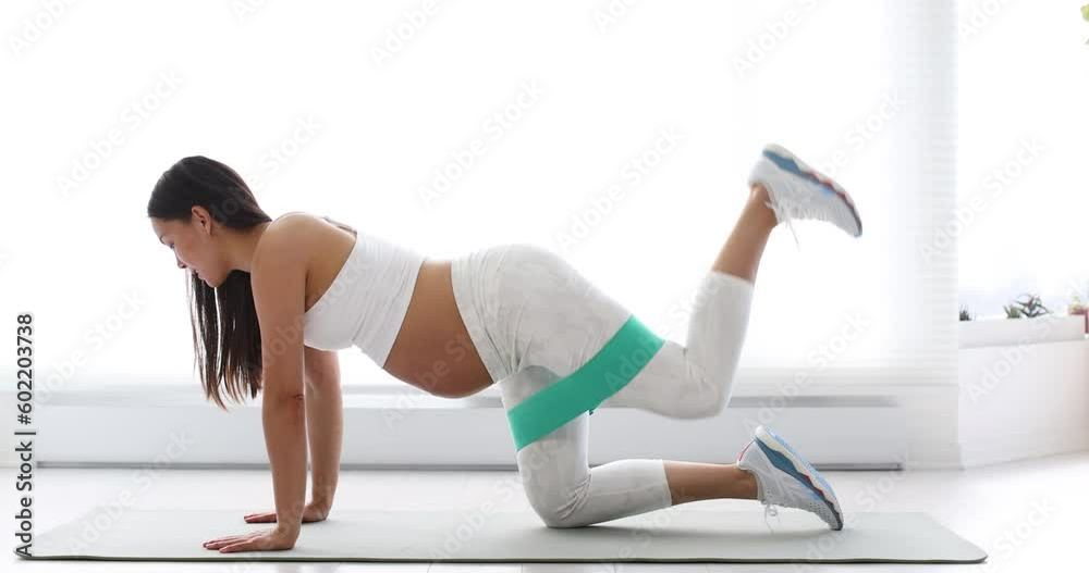 Prenatal Workout. pregnant woman training resistance band fitness doing leg workout donkey kick floor exercises with elastic band. Glute muscle activation with leg raise kickback