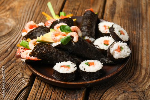 Plate with tasty sushi cones and rolls on wooden background
