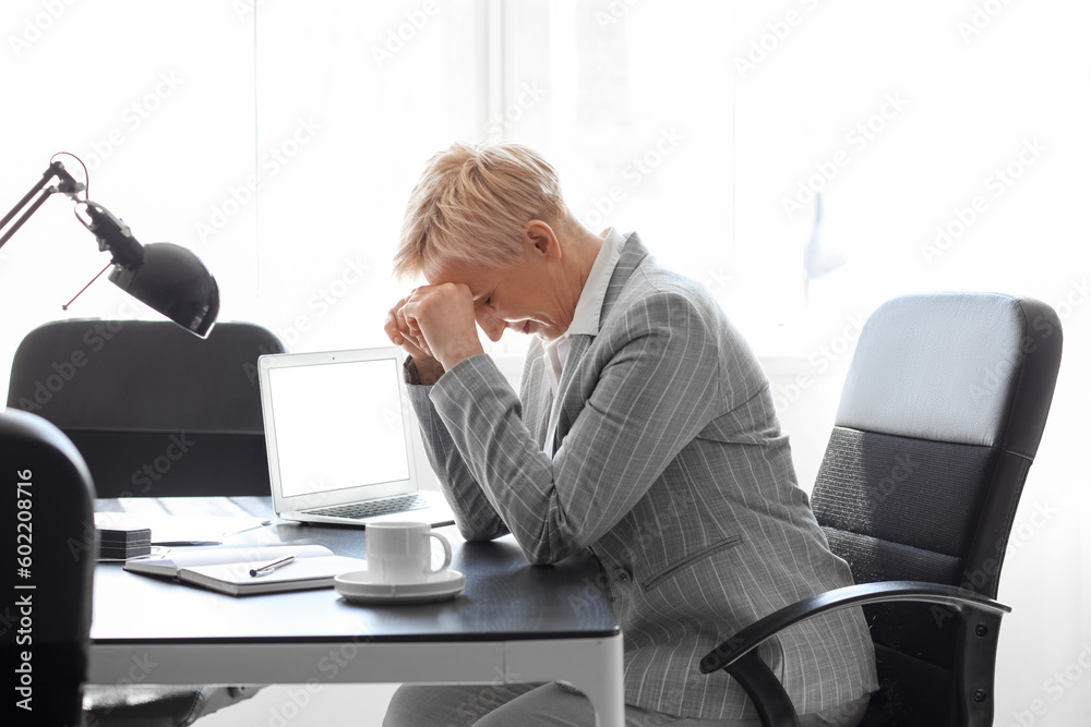Tired mature businesswoman sitting at table in office Tired mature businesswoman sitting at table in office