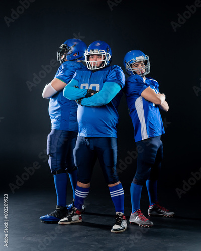 Portrait of three men in blue American football uniforms standing with their arms crossed over their chests on a black background. 