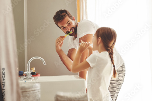 Dental care, father with daughter brush their teeth and in bathroom of their home. Oral hygiene routine, parent with child use toothbrush for health and wellness mouth protection in the morning photo