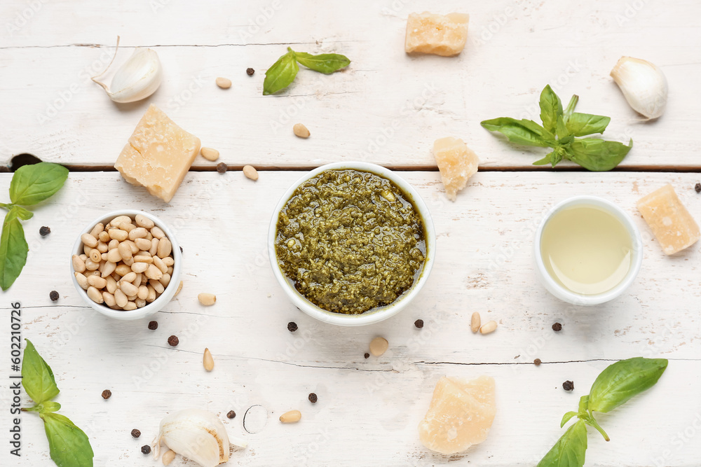 Composition with bowl of delicious pesto sauce and ingredients on white wooden table Composition with bowl of delicious pesto sauce and ingredients on white wooden table