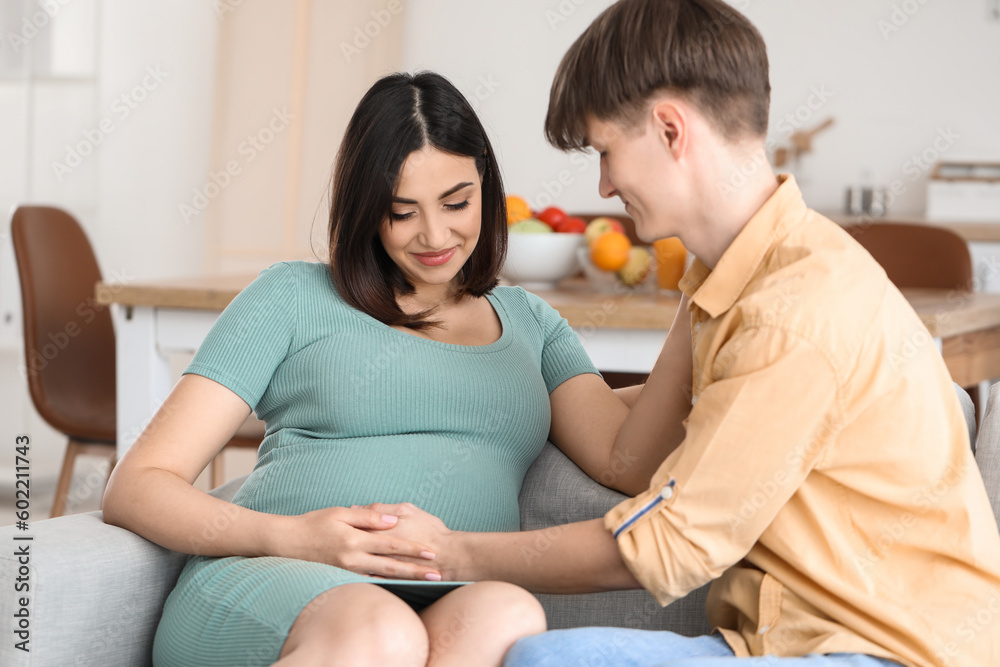 Young pregnant couple sitting on sofa at home Young pregnant couple sitting on sofa at home