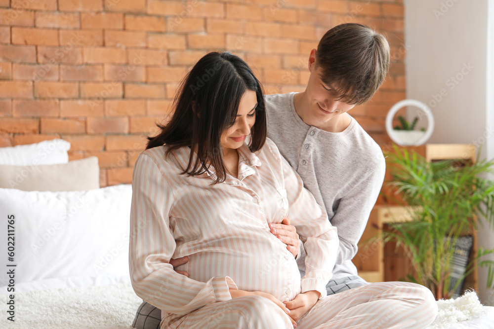 Young pregnant couple sitting in bedroom Young pregnant couple sitting in bedroom