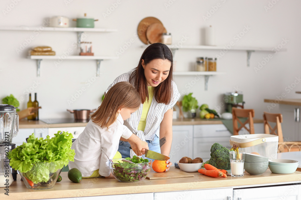 Little girl with her mother cutting orange in kitchen