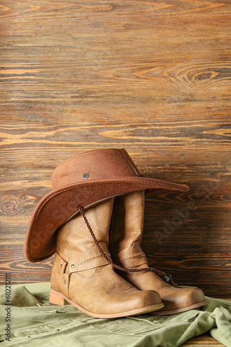 Cowboy boots, hat and shirt on wooden background