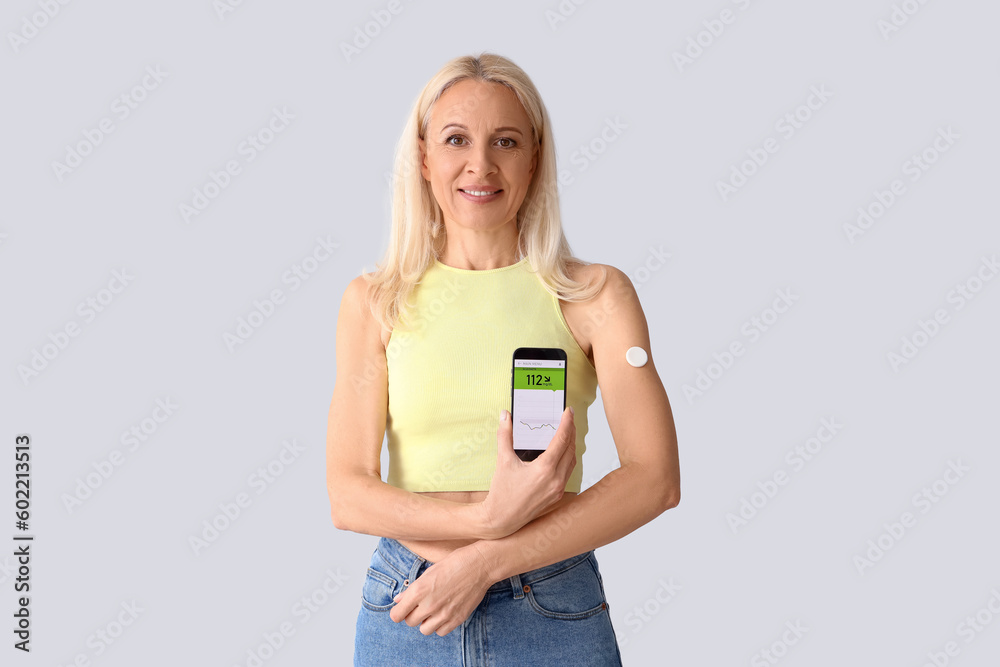 Mature diabetic woman with mobile phone measuring blood sugar level on light background Mature diabetic woman with mobile phone measuring blood sugar level on light background