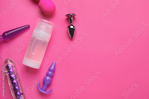 Bottle of lubricant with vibrators and anal plugs on pink background