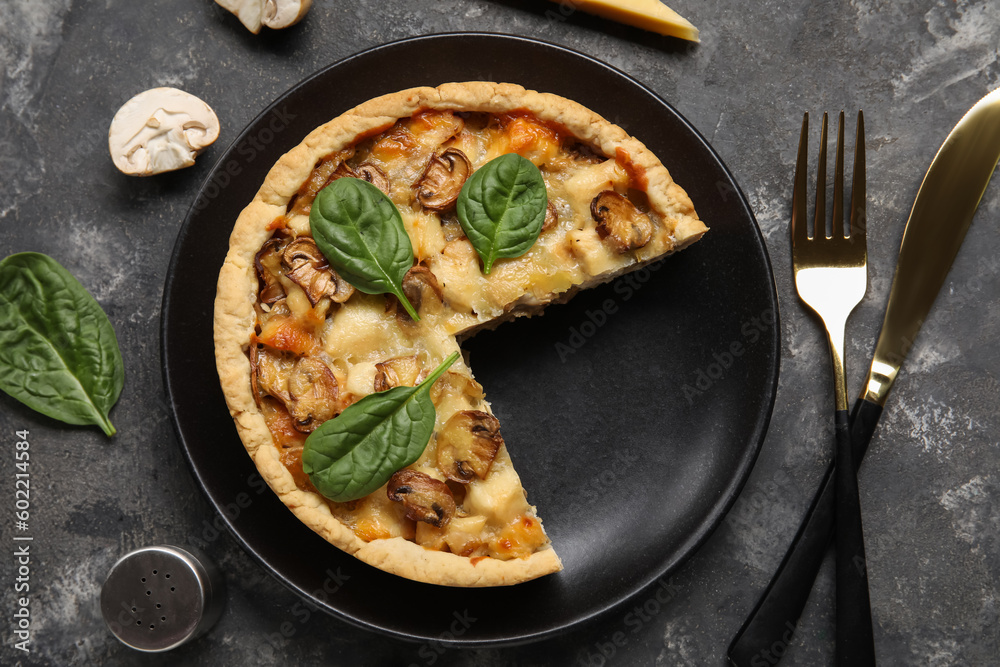 Mushroom pie with spinach leaves and cutlery on black grunge table