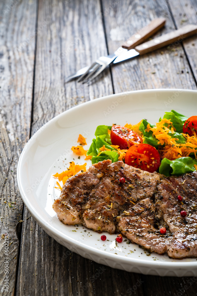 Grilled pork steaks with fresh vegetable salad on wooden table Grilled pork steaks with fresh vegetable salad on wooden table