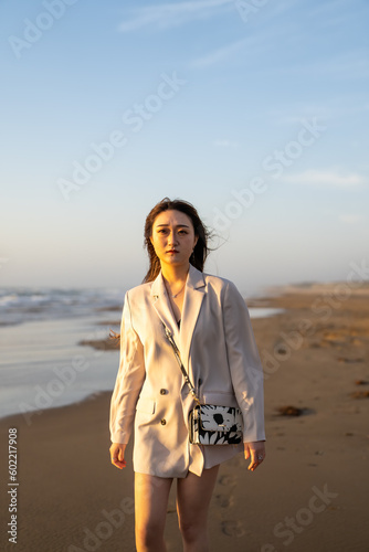                                                                                                                                      A young woman in a white jacket with a smartphone walks on chirihama beach at sunset in Hakui  Ishikawa  Japan