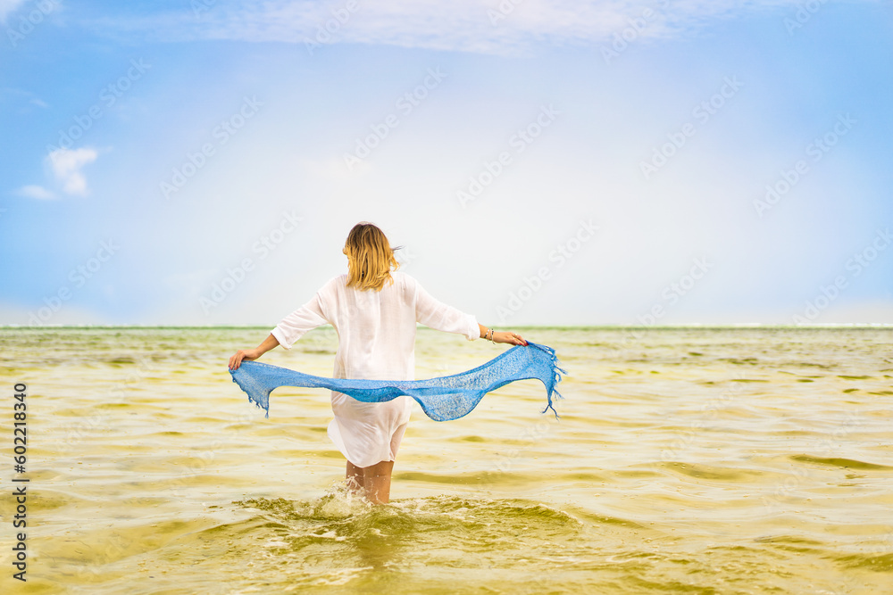 Beach holiday - beautiful woman holding shawl walking on sunny, tropical beach
