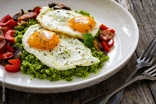 Breakfast - sunny side up eggs, grated broccoli, stir fried vegetables and sliced sausages served on wooden table

