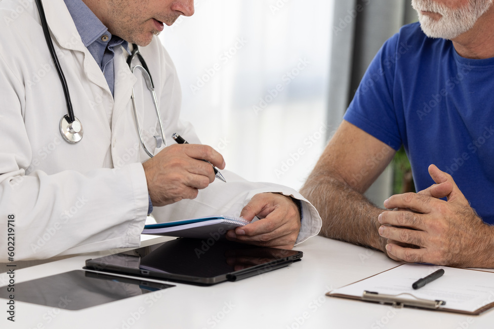 Doctor holding pen and writing patient history list or prescription on note pad and talking to elderly patient about medication and treatment Doctor holding pen and writing patient history list or prescription on note pad and talking to elderly patient about medication and treatment