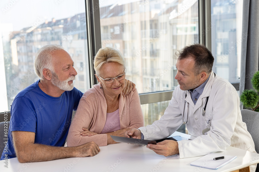 Obraz premium Healthy smiling senior couple feeling cheerful about good news at medical consultation. Happy eldelrly man and woman talking to a doctor at appointment.