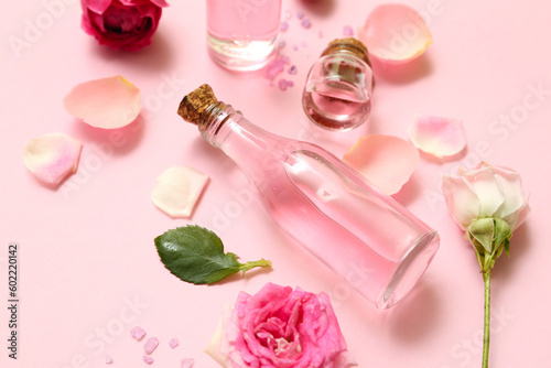 Bottles of cosmetic oil with rose extract and flowers on pink background
