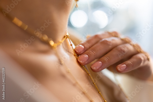Chic girl with a beautiful manicure, graceful neck, and velvety skin gently touches a gold chain with her finger in a jewelry store. The woman advertises a gold necklace in a luxury boutique.