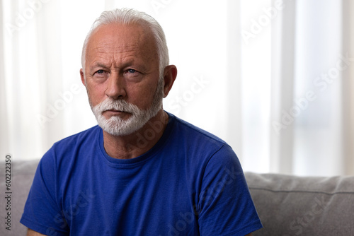 Pensive elderly mature senior man sitting on sofa looking away.