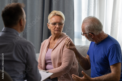 Unhappy senior couple arguing, having fight, disagreement at psychologists office. Frustrated elderly wife and husband discussing relationship problems with their therapist