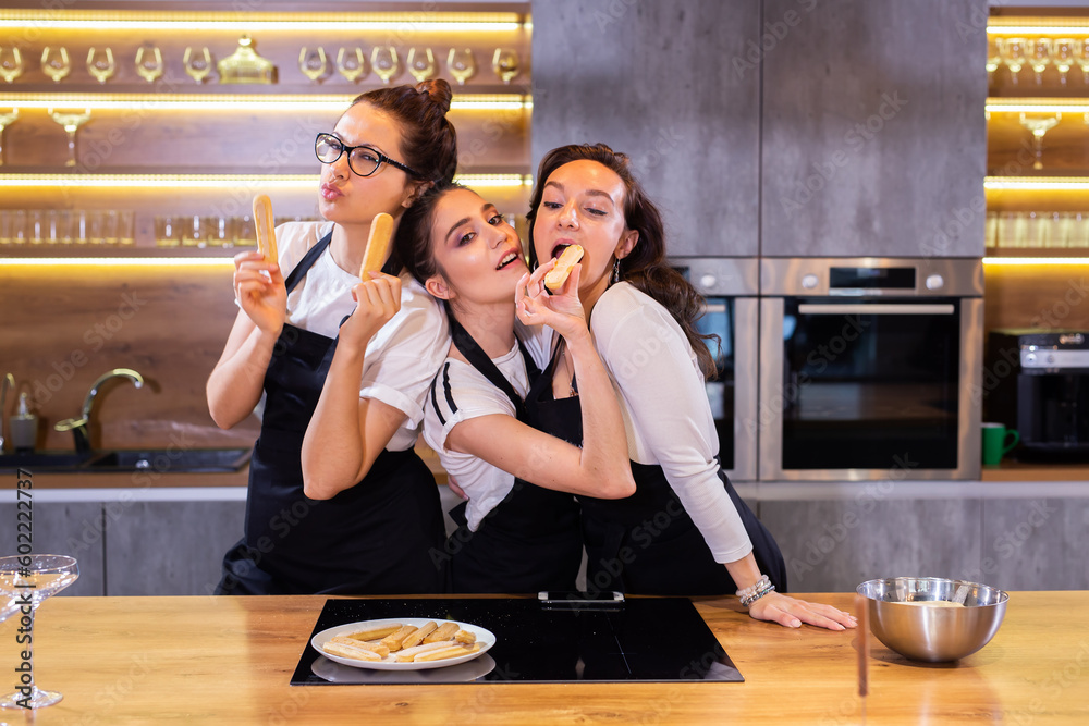 Three funny female chef in uniform holding cookies while smiling and having fun at camera in the kitchen Three funny female chef in uniform holding cookies while smiling and having fun at camera in the kitchen