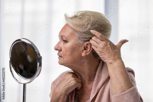 Bilde på lerret Senior woman checking her hairline or grey hairs by looking at mirror
