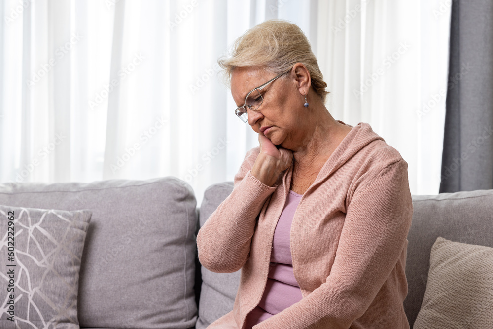 Senior woman suffering from neck pain sitting on sofa at home Senior woman suffering from neck pain sitting on sofa at home