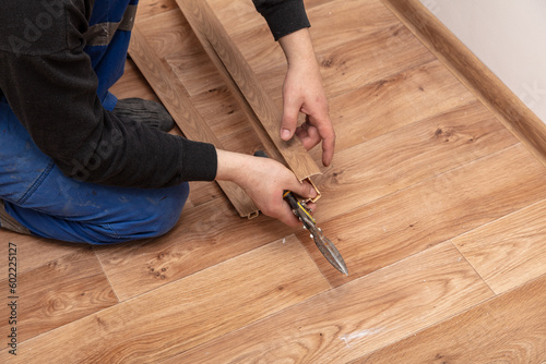 A worker installs a skirting board on the floor in a room