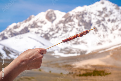 hand hold Arrosticino - typical Abruzzese sheep skewer - grilled with mountains of Gran Sasso background in Campo Imperatore plain