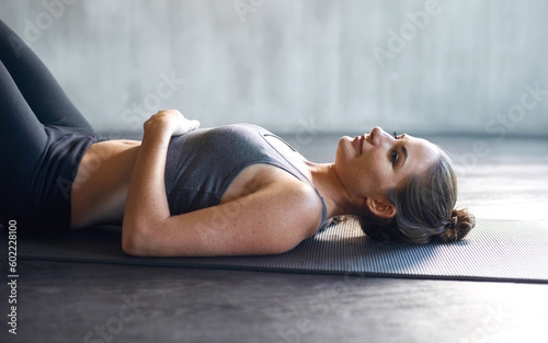 Gym, floor and tired woman relax after training, cardio and intense workout routine. Fitness, fatigue and girl on the ground at sports center after pilates, exercise or yoga for health and wellness