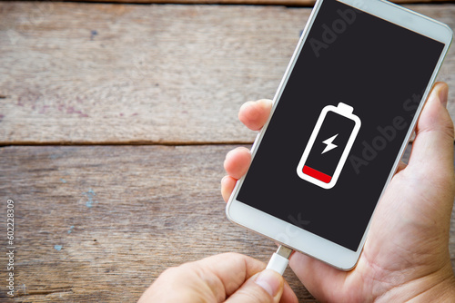 Close up a man hands plugging a charger on a smart phone on a wooden table