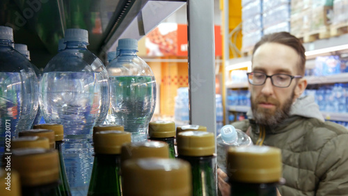 Many various bottles of water in a store and a male buyer holding one reviewing
