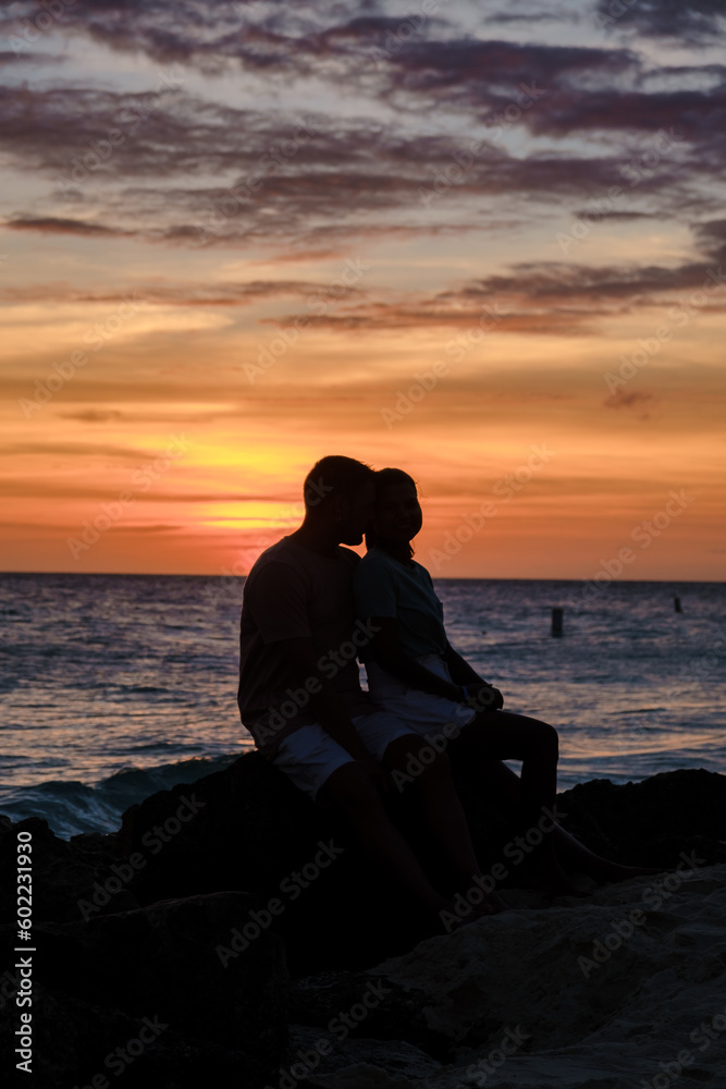 A couple of men and women are on the beach watching the sunset during vacation at Aruba Island Caribbean. man and woman by the ocean during susnet 