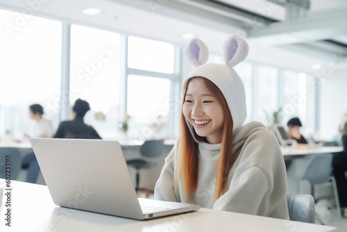 A business-focused Asian girl works on her laptop in a modern co-working space, while wearing a fun rabbit knit hat that adds a touch of unique style. generative AI.
