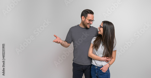 Obraz na plátne Cheerful romantic young boyfriend with arm around embracing girlfriend while standing against background