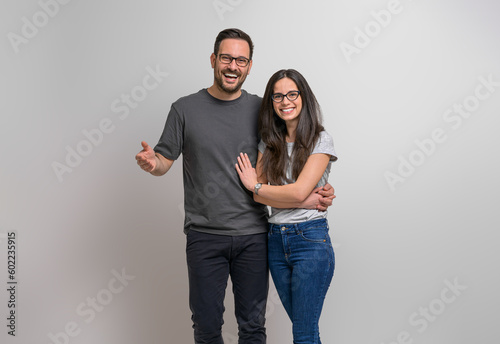 Portrait of cheerful romantic young couple holding hands and looking at camera. Joyful boyfriend and girlfriend wearing eyeglasses and casuals smiling and posing against background