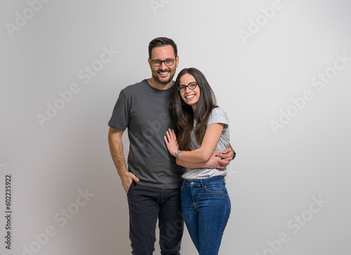 Portrait of affectionate young girlfriend and boyfriend holding hands and standing happily against background. Cheerful couple wearing eyeglasses embracing and looking at camera