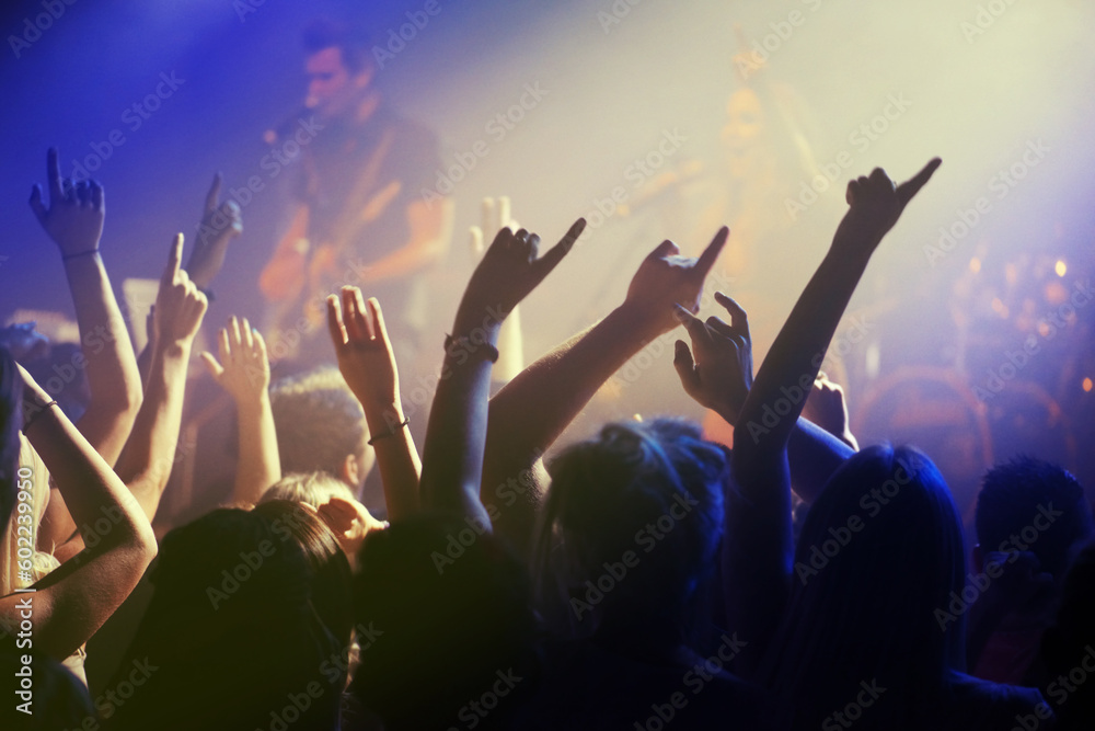 Hands in air, people dancing at concert or music festival with neon lights and energy at live event. Dance, fun and excited crowd of fans in arena for rock band, musician performance and spotlight.