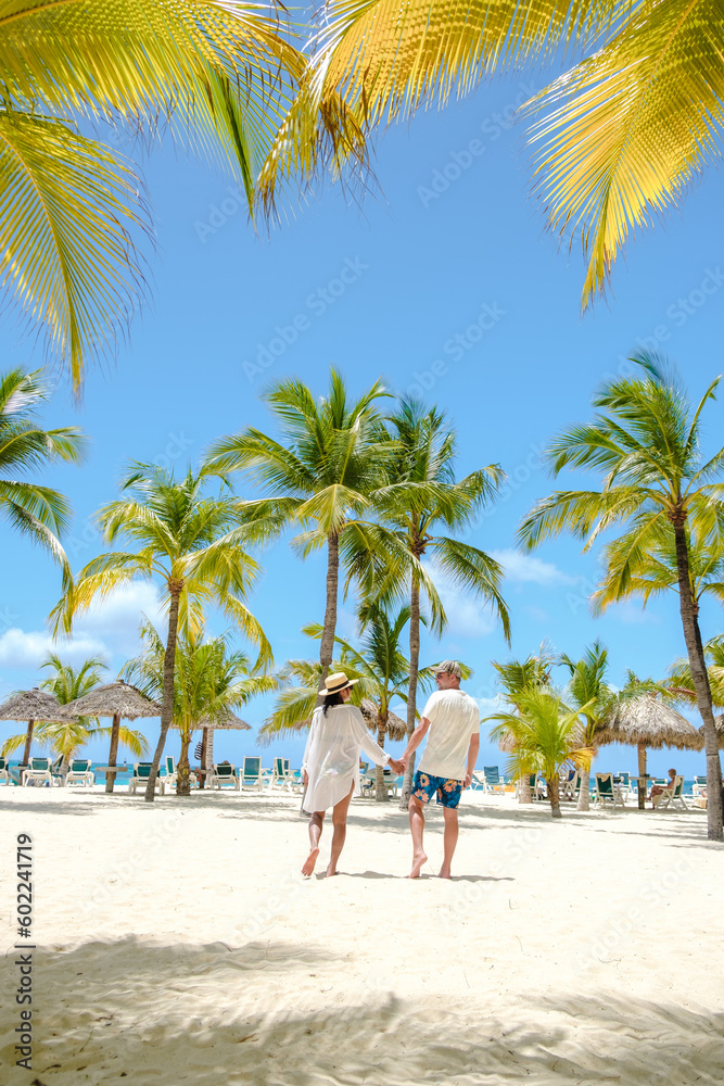 Fototapeta premium Palm Beach Aruba Caribbean, a couple of men and women at a white long sandy beach with palm trees at Aruba Antilles.