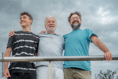 Portrait of charming family group bonding hugging, grandfather with middle aged son and young teenage grandson outdoors smiling carefree