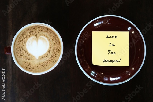 Coffee cup and handwritten note note LIVE IN THE MOMENT, concept of live with the present - be with the NOW not past or future, control anxiety - not to worry about yesterday or tomorrow