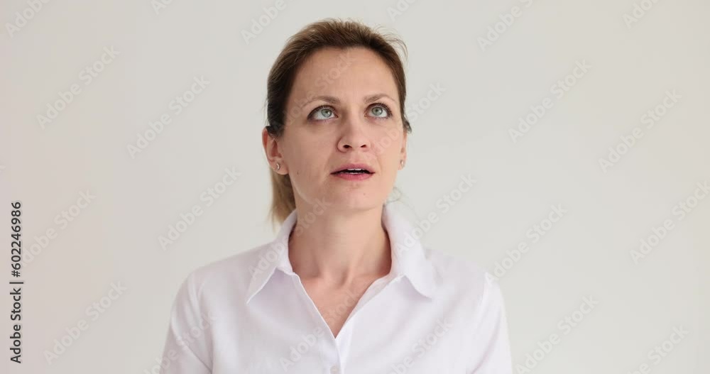 Woman in light shirt stands and looks upward at room ceiling. Female person follows object while standing on white background slow motion Woman in light shirt stands and looks upward at room ceiling. Female person follows object while standing on white background slow motion