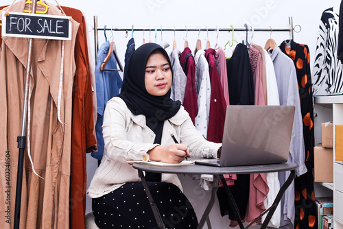 Muslim woman seller and busissnes owner checking clothes stock in store and writing data in notebook photo