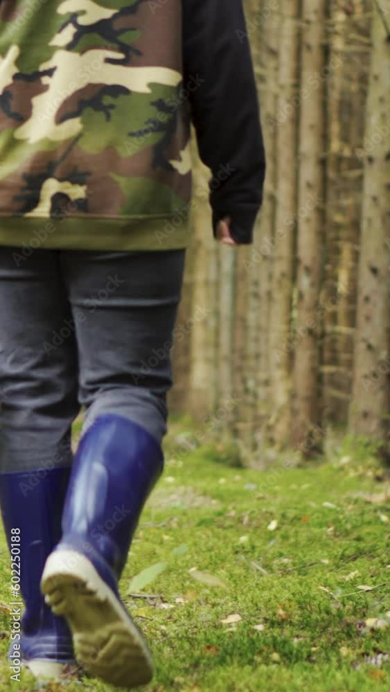A young woman in a camouflage jacket walks through the woods with a basket. Looking for mushrooms. Vertical video. A young woman in a camouflage jacket walks through the woods with a basket. Looking for mushrooms. Vertical video.