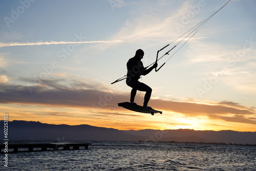 silhouette of a person doing a kite surfing freestyle acrobatic jump at sunset. Summertime sport