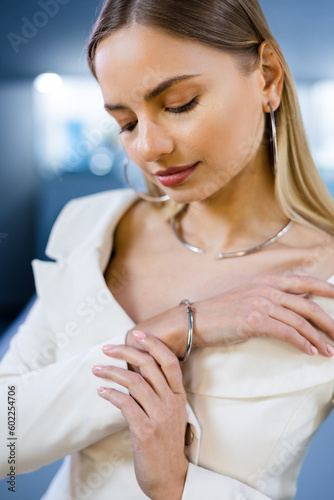 Gold and diamond bracelet adorns the wrist of an elegantly glamorous model girl in a luxury jewelry boutique. The woman showcases beautiful diamond accessories in the jewelry salon.