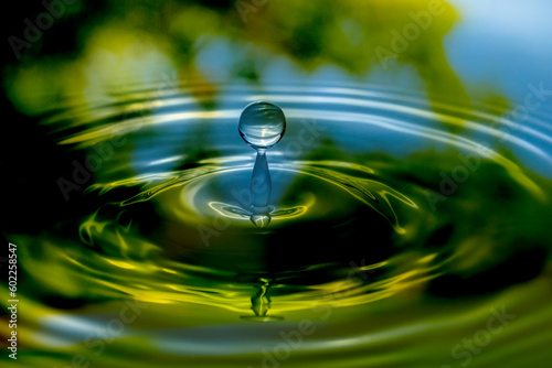 Water drop falling into nature surface. Liquid ripple splash in sunlight with reflection. Graphic design element for poster, package, flyer, abstract background