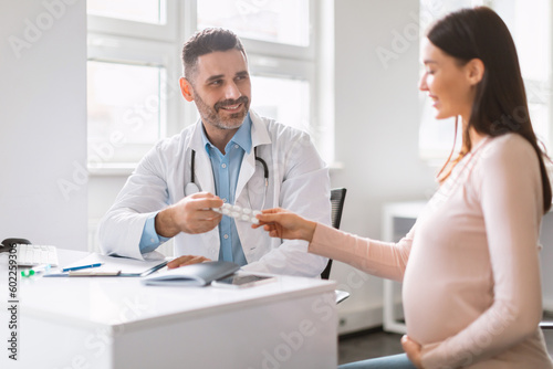 Pregnancy nutrition. Male specialist giving vitamins or supplements to young pregnant woman, doctor prescribing pills
